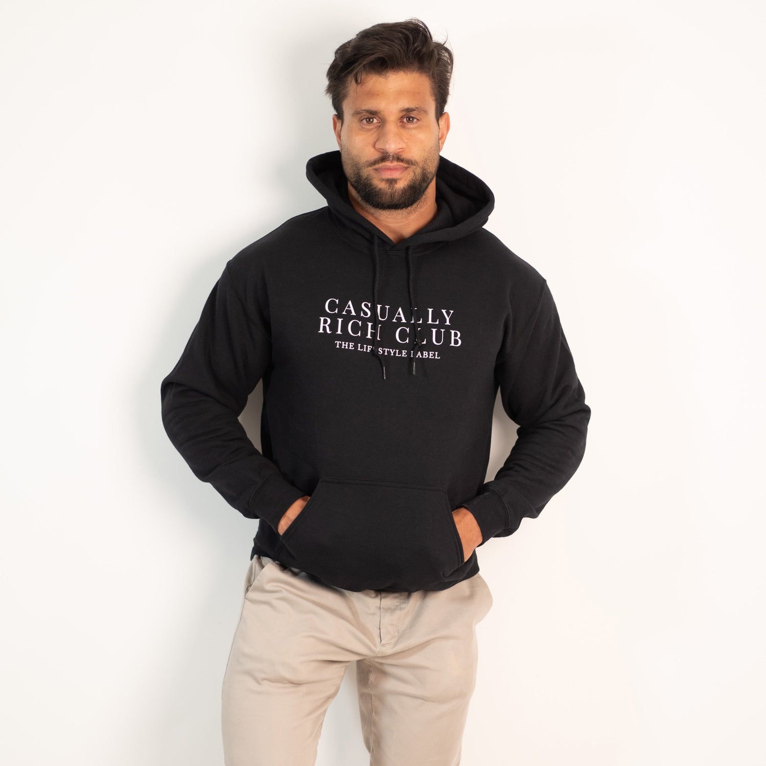 Man wearing a black hoodie with text, beige pants, and white sneakers on a white background